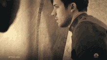 a man looking out a window with the nbc logo on the bottom