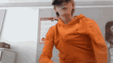 a person wearing an orange hoodie is standing in front of a wall with a sticker that says winner out