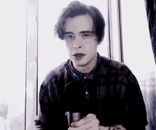 a young man in a plaid shirt is holding a microphone in his hand
