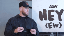 a man in a black jacket stands in front of a sign that says hey ( ew )