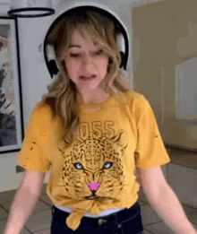 a woman wearing headphones and a yellow shirt with a leopard on it is standing in a room .