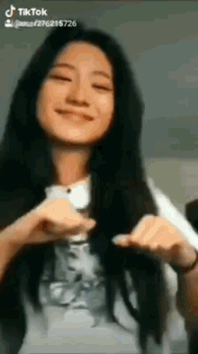 a woman with long black hair is smiling and making a funny face while wearing a white shirt .