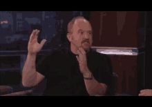 a man with a beard is sitting at a table with his hands outstretched and a watch on his wrist .