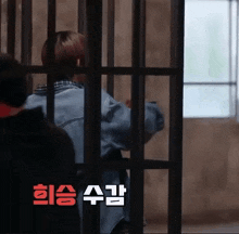 a man is behind bars in a jail cell with korean writing on the bottom