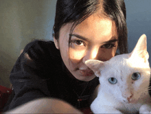 a woman is holding a white cat that has blue eyes