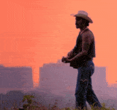 a man in a cowboy hat holds a guitar in a field