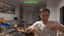 a man sitting on a couch in a living room with a green screen that says kick.com/ajemgei