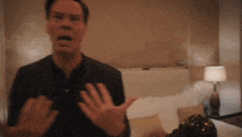 a man in a black shirt is making a funny face in a bedroom