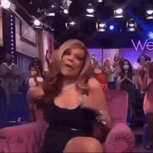 a woman in a black dress is sitting on a pink couch in front of a sign that says wendy .