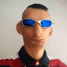a man wearing sunglasses and a red and white shirt is looking at the camera .