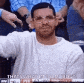 a man wearing glasses and a sweater is sitting in a crowd of people .
