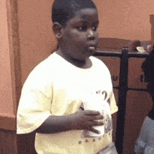 a young boy in a yellow shirt is holding a cup of coffee .