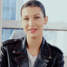 a woman wearing a black leather jacket and hoop earrings is smiling