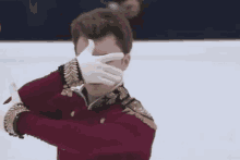 a man in a red jacket is covering his face with his hands .