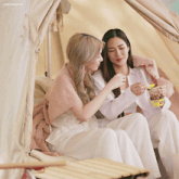 two women are sitting next to each other and one is holding a cup of rice