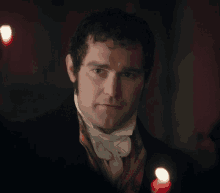 a man in a suit and tie is standing in front of candles