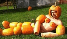 a man is laying on the grass surrounded by pumpkins .