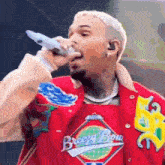 a man in a red jacket is singing into a microphone while wearing a breezy bow shirt .