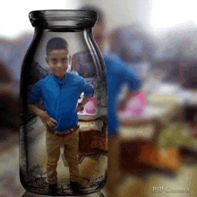 a young boy in a blue shirt is standing inside of a glass bottle .