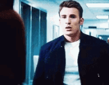 a man in a black jacket and white shirt is standing in a hallway .