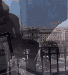 a man sits on a balcony looking out at a city with a tablet in front of him