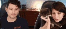 a man wearing a deviant shirt holds a cat in his hands
