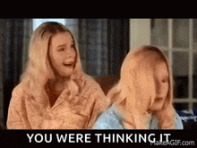 two blonde women are sitting next to each other on a couch and talking .