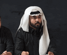 a man with a beard is wearing a black shirt and a white head scarf