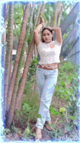 a woman in a crop top and jeans stands in front of trees