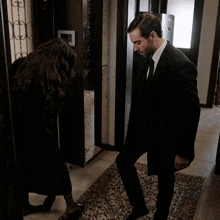 a man in a suit stands next to a woman in a black coat in a hallway