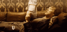 a man is laying on a couch reading a book with the letter u below him