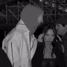 a man in a hooded jacket stands next to a woman in a black dress