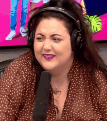 a woman wearing headphones and a polka dot shirt is smiling and talking into a microphone .