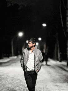 a man wearing a grey jacket and a white shirt walks down a street at night