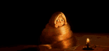 a cartoon girl with long hair is wrapped in a blanket in a dark room next to a candle