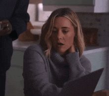a woman in a gray sweater is looking at a tablet .