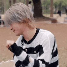 a young man wearing a black and white striped sweater is sitting on the ground eating a sandwich .