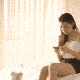 a woman is sitting on a bed using a cell phone .