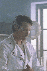 a man in a white coat is smoking a cigarette in a room .