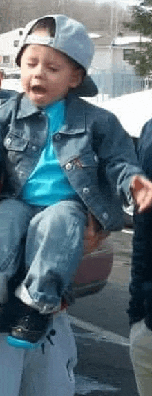 a little boy wearing a hat and a denim jacket is being carried by a person .