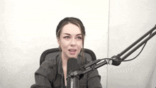 a woman is talking into a microphone while sitting in front of a white wall .