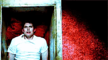 a man in a white shirt is sitting in a doorway in front of a red wall