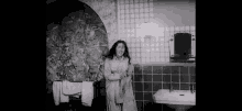 a black and white photo of a woman standing in a bathroom .