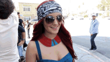 a woman with red hair wearing sunglasses and a headband is smiling in front of a sign that says mexico.com