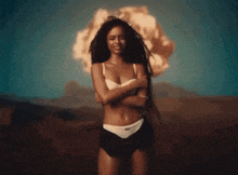 a woman in underwear stands in front of an explosion in the desert