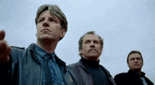 three men are standing in front of a blue sky and one man is pointing