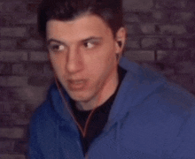 a young man wearing headphones and a blue hoodie is looking at the camera .