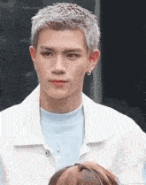 a young man with gray hair is wearing a white jacket and a blue t-shirt .