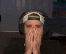 a man wearing headphones and a hat covering his face with his hands .