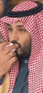 a man with a beard wearing a keffiyeh and a scarf is smoking a cigarette .